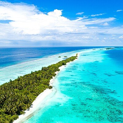An aerial shot of a narrow island covered by tropical trees  in the middle of the sea in Maldives