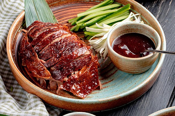 side view of traditional asian food peking duck with cucumbers and sauce on a plate